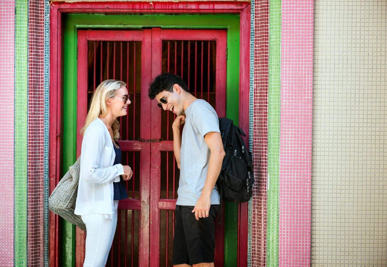 A man and a woman stand infront of a door that is brightly colored pink and green.