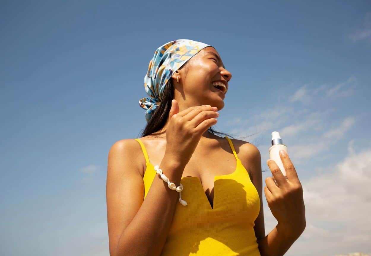 A woman in a bathing suit smiles as she applies sunscreen from a white bottle.