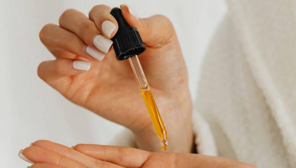 Female hands one with a oil dropper dropping oil from it into her other hand,