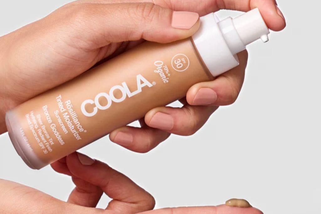 a woman's hands holding a tan bottle and pumping a bit of the sunscreen onto her finger.