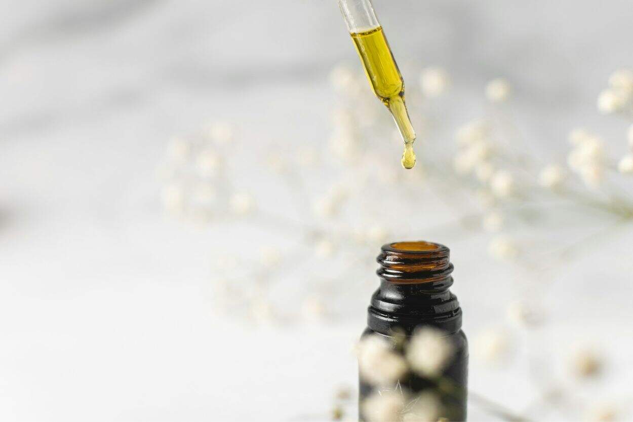 A brown bottle with a dropper of oil above it.